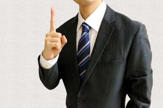 人差し指を立てるスーツを着た男性の画像