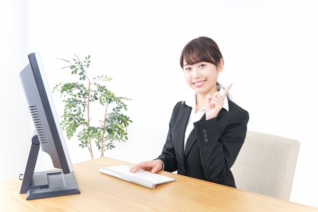 パソコンで作業をしながら人差し指を立てる女性営業マンの画像
