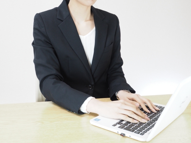 パソコンでメールを打つスーツを着た女性の画像