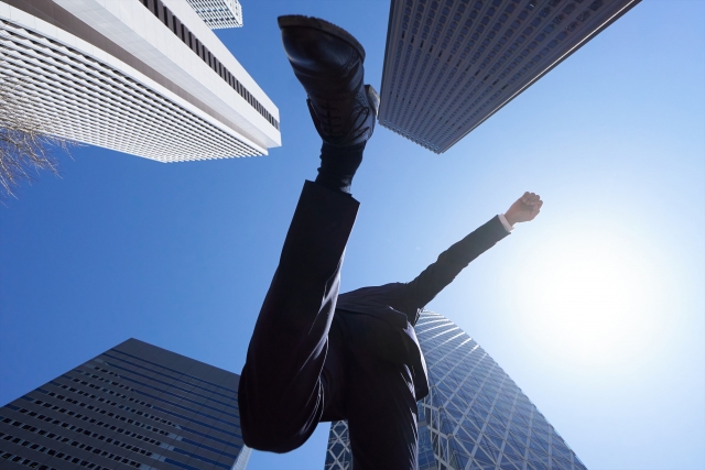 オフィス街でジャンプする男性営業マンの画像